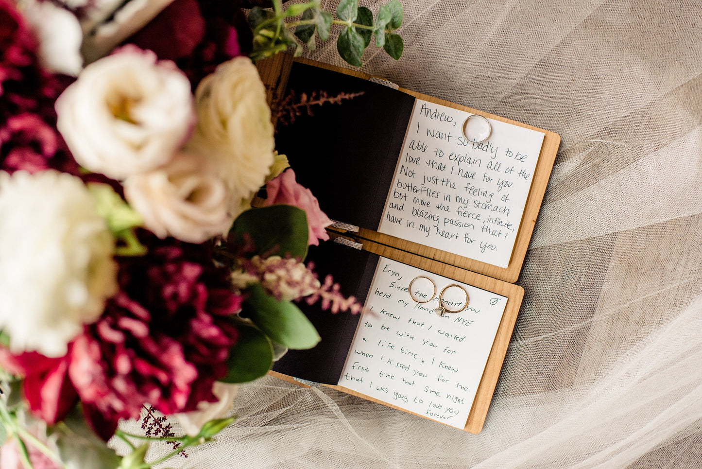 Two vow books lie open with golden rings and a beautiful bouquet in the background.