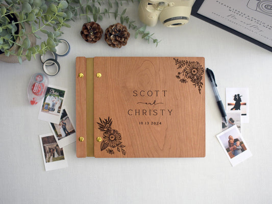 Custom cherry wood wedding guest book with an engraved floral sunflower design. Gold screws and gold leather binding. Surrounded by Polaroid photos, a pen, and photo tape, perfect for capturing special memories at weddings and significant events